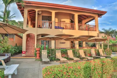 a patio with chairs and umbrellas in front of a house at The Backyard Beachfront Hotel in Jacó