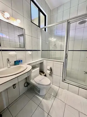 a white bathroom with a toilet and a sink at The Backyard Beachfront Hotel in Jacó