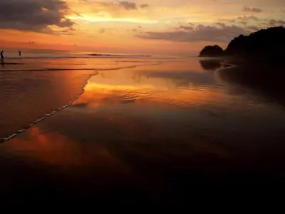 a person walking on the beach at sunset at The Backyard Beachfront Hotel in Jacó