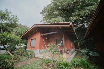 a small red house with a porch in a yard at Lodge Mirador - Great Swimming pool - Kitchen - BBQ - Netflix in Tajo Alto