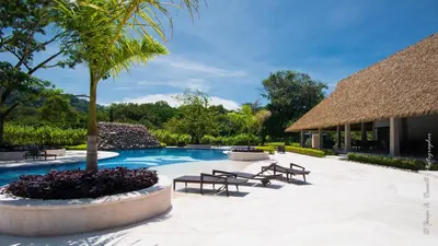 a resort with a swimming pool with benches and trees at Ciudad del Mar 126 condo in Jacó