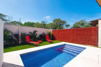 a backyard with a swimming pool and red chairs at Pop House with private pool at Ciudad del Mar in Jaco in Jacó