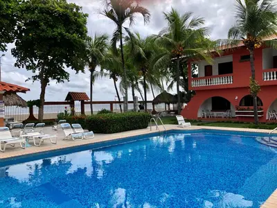 a large swimming pool next to a building with palm trees at Apartotel Flamboyant in Jacó