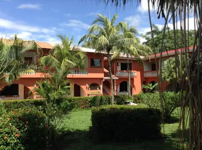 an orange building with palm trees in front of it at Apartotel Flamboyant in Jacó