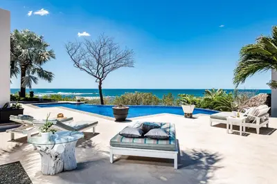 a patio with chairs and a pool with the ocean at The Point Luxury Villa, Tamarindo in Tamarindo