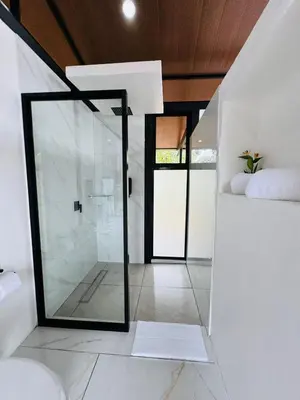 a bathroom with a glass shower and white walls at Cabañas La Hermosa #1 in Guápiles
