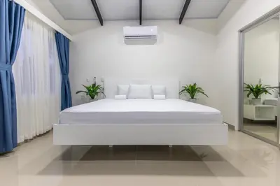 a white bedroom with a white bed and blue curtains at The Zion Suite Tortuguero in Tortuguero