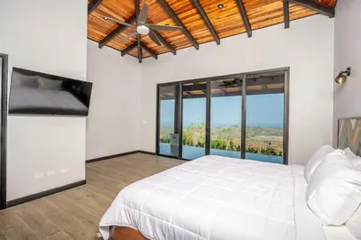 a bedroom with a white bed and large windows at Luxurious Mountaintop Retreat with Ocean Views in Matapalo