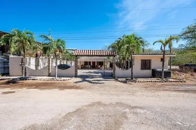 a house with palm trees in front of a fence at Cozy Seaside Studio Perfect for Families in Playa Grande