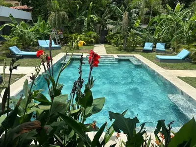 a pool in a garden with blue chairs and a red flower at Hotel Good Life in Coco