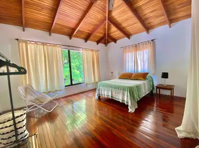 a bedroom with a bed and wooden floors and windows at Lofty, fully equipped apartment in the heart of Montezuma in Puntarenas