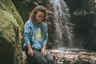 a woman sitting on a rock in front of a waterfall at Santuario Ecologico Monteverde in Monteverde Costa Rica