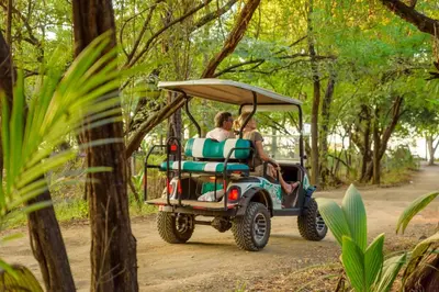 two people in a golf cart driving down a dirt road at Villa Maravilla Estates, Tamarindo Beach, Prime Location, Family & Friends in Tamarindo