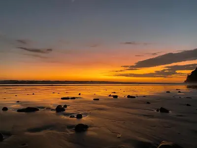 a sunset on a beach with rocks in the sand at Rustic wooden little house close to the beach in Uvita