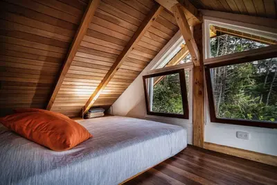 a bed in a room with two windows at Casita Acantilado - Timber Frame Tiny House in Monteverde Costa Rica