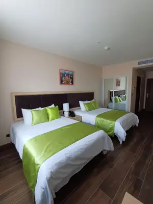 two beds in a hotel room with green sheets at Hotel Puerto Limón CR in Puerto Limón