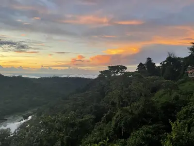 a sunset in the mountains with a river and trees at Volcan Hule Lodging in Río Cuarto
