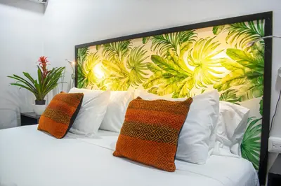 a bed with orange and white pillows and a floral wall at Bukala Village Lodge in San Ramón