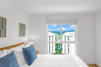 a white bed with blue pillows in front of a window at Upstay - New Condo in Jaco - 5 mins from Beach in Jacó