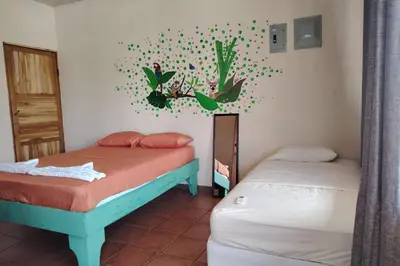 a bedroom with two beds and a wall with a mural at Hospedaje Papalotes in Quepos