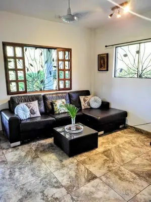 a living room with a black couch and a table at CASA TROPICAL-3 bdrm w private pool Close to beach in Esterillos