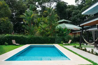 a swimming pool with two chairs and a house at TAMANDUA HOMES el centro de Uvita in Uvita