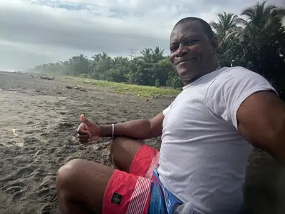 a man sitting on the beach giving a thumbs up at Miss Miriam BeachFront Cabins in Tortuguero