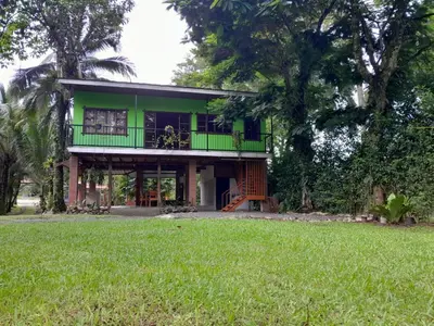 a green house with a green balcony and a yard at Riverside Oasis Cabin with A C in Guápiles