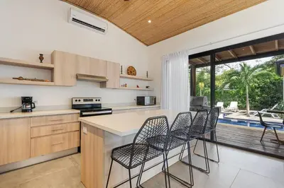 a kitchen with chairs and a counter with a table at CU28 New 3 Bdrm Home w Pool and Guanacaste Tree in Tamarindo