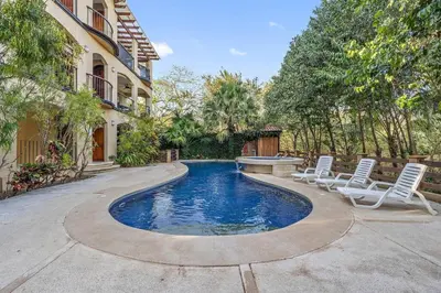 a swimming pool with two chairs and a table at Gav10 Modern Pool Side Condo in Quiet Area of Tam in Tamarindo