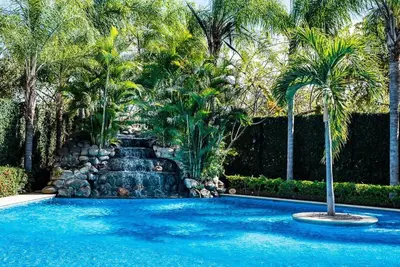 a swimming pool with a waterfall and palm trees at Nax3 Luxury Condo in Upscale Langosta Community in Tamarindo