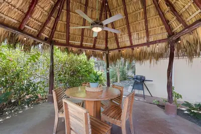 a wooden table and chairs under a straw umbrella at VBM1 Beachside Cottage Steps from the Shore in Tamarindo