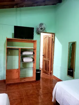 a room with a tv and a shelf with towels at Arenal Hostel La Catarata in Fortuna