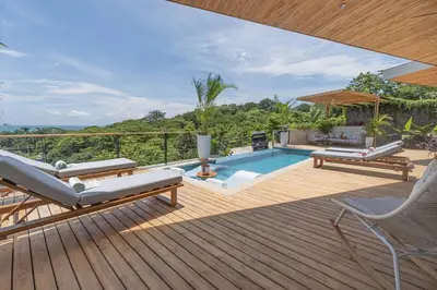 a wooden deck with a swimming pool and chairs and avisor at Blanko Mar Ocean view in Santa Teresa Beach