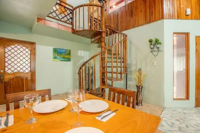 a dining room with a wooden table and a spiral staircase at Arenal Family Home - Families & Friends Gateway in Fortuna