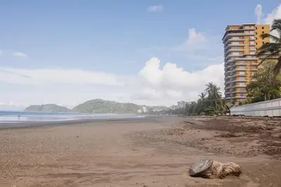 a beach with a rock on the sand and a building at In the HEART of Jaco at Villas Paraiso in Jacó