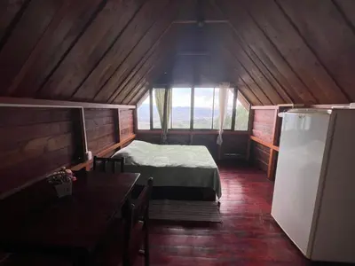 a room with a bed and a table and a refrigerator at Vista Hermosa Lodge in Aserrí