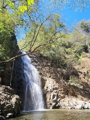 a waterfall on the side of a mountain with a river at Cabinas Guacamaya in Cabuya
