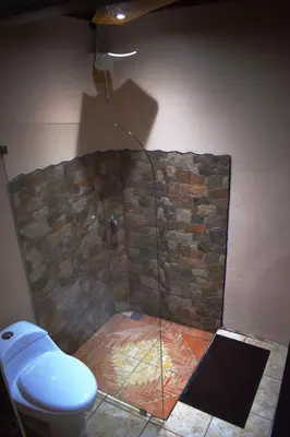 a bathroom with a toilet and a stone wall at Hospedaje Casa Coyote in Hacienda Monteverde