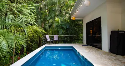 a swimming pool with two chairs and trees at Four Winds Properties A Short Walk to the Beach in Nosara