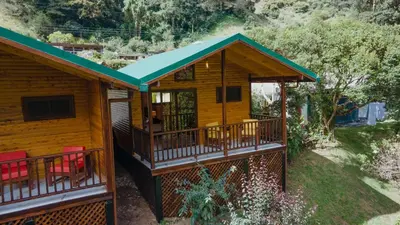 a log cabin with a deck and red chairs at Cabinas El Quetzal in San Gerardo de Dota
