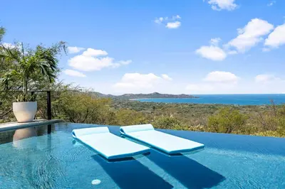 a swimming pool with two lounge chairs and the ocean at Infinity Edge Pool Oceanview 4 BR 4BA in Brasilito