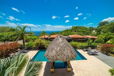 a resort with a swimming pool and a straw umbrella at Captivating Ocean Views Condo with Pool in Ocotal
