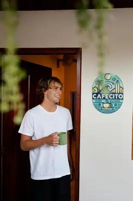 a man holding a green cup in front of a door at The Cafecito Surfhouse - Santa Teresa in Santa Teresa Beach