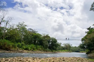 two people crossing a suspension bridge over a river at Selva Verde Lodge in Sarapiquí