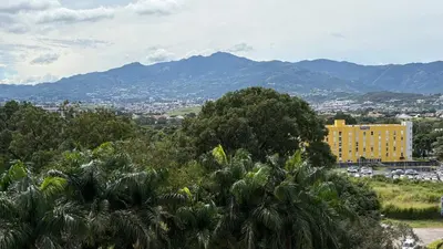 a yellow building in front of a city with mountains at Luxury apartment 10 min to Airport Be Cariari Condo #402 in La Asunción