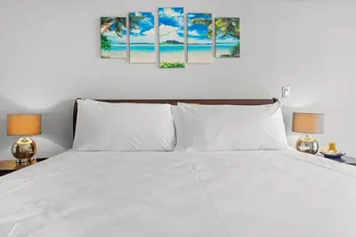 a bedroom with a white bed with three paintings on the wall at Majestic Oceanview Condo with King Beds in Coco