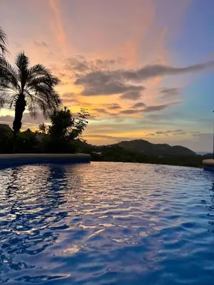 a swimming pool with a palm tree and a sunset at Majestic Oceanview Condo with King Beds in Coco