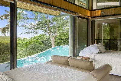 two beds and a couch in a room with a large window at Villa La Loma, Oceanview, Private Pool and AC! in Tarcoles