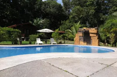 a swimming pool with two chairs and an umbrella at Hotel Brisas del Rio Guápiles in Jiménez